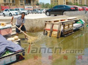 　　老許在小區(qū)門口賣蔬菜，因污水冒出太多淹了菜攤，他不得不清理腳下的污水