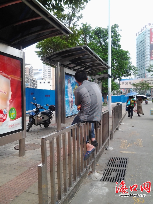 一男子坐在公交站护栏上候车
